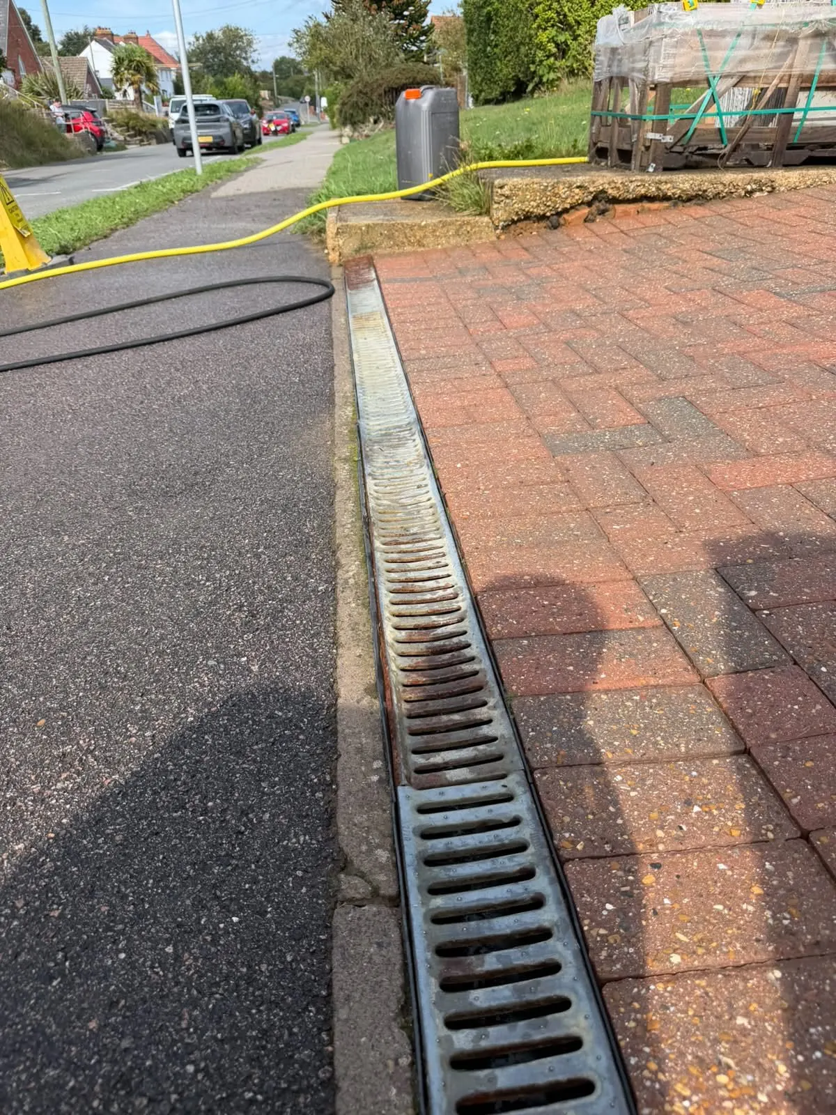 The same drainage channel after clearing, with weeds removed and the red block-paving edge cleaned