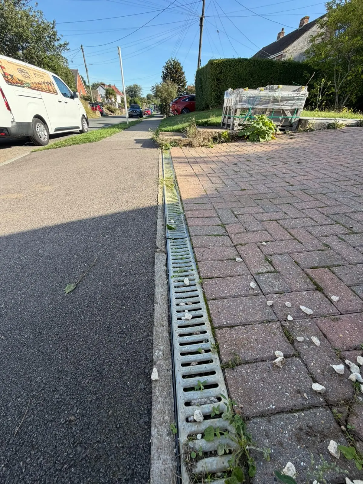 Driveway drainage channel before clearing, with weeds and build-up along the channel and paving edge