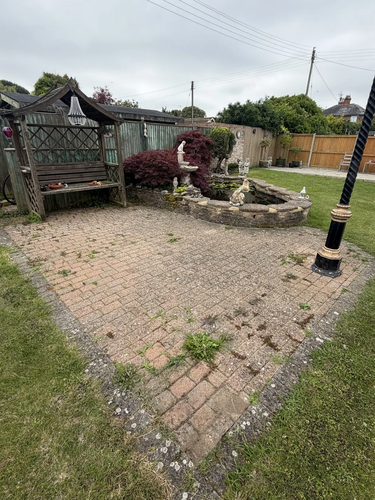 Garden block-paved patio before cleaning, with moss, weeds and green growth across the paving and joints