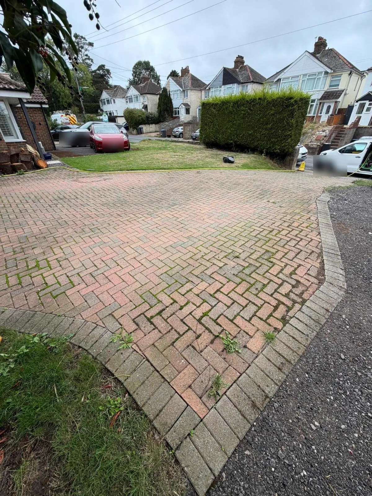 Large herringbone block-paved driveway before cleaning, with green growth in the joints and dull red blocks